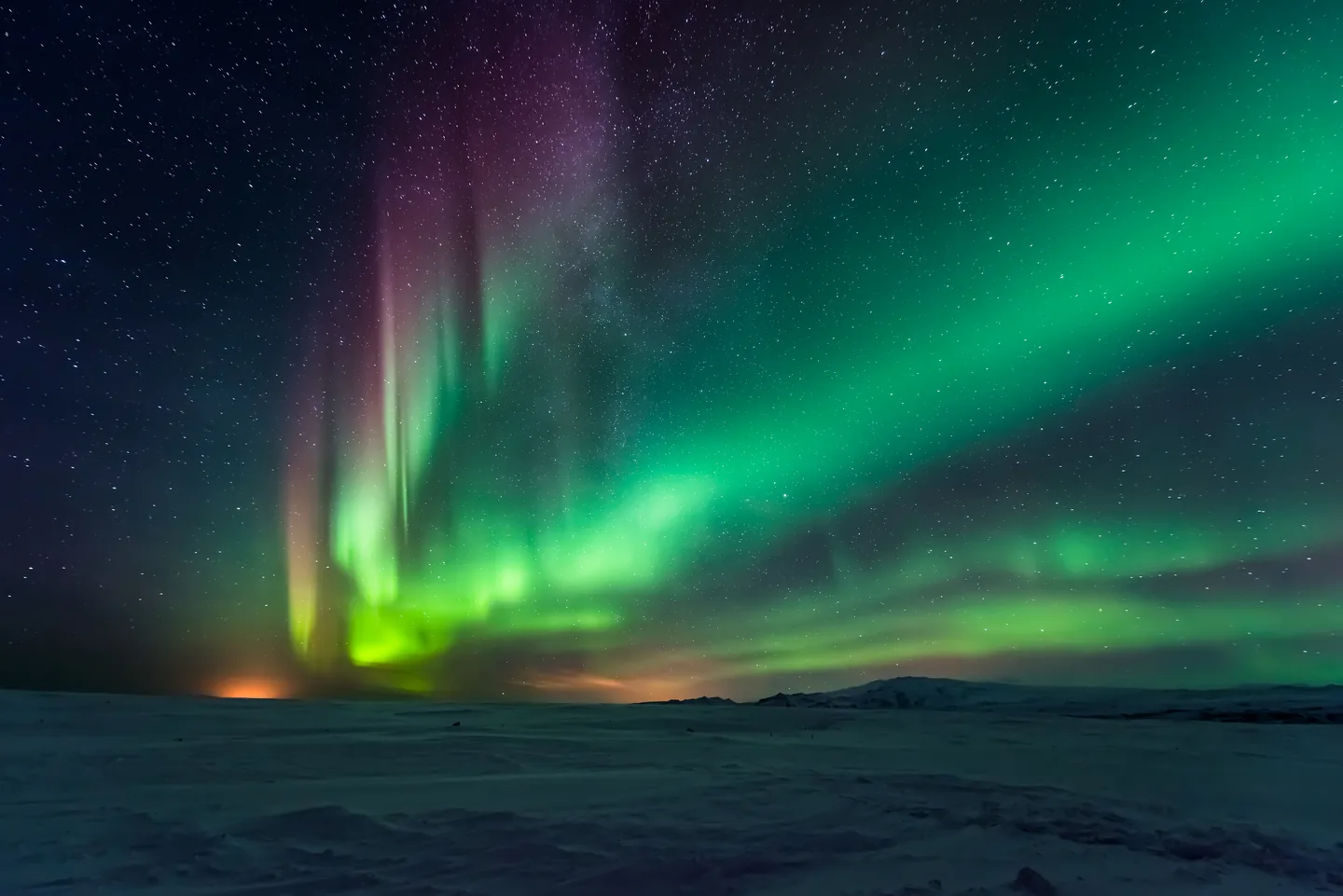 Green and purple aurora above a dark snow-covered landscape.