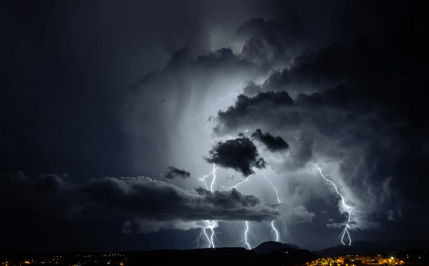 Lightning beneath dark storm clouds above a city at night.